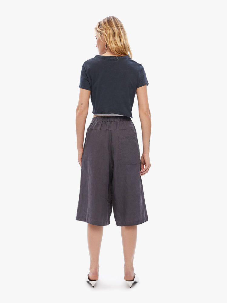 Back view of a woman in Elsa Esturgie uses natural fabrics, these wide-leg capri pants have a high rise gathered waistband, side pockets and an airy feel made from 100% linen in a dark grey hue