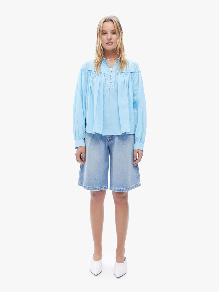 Front full body view of a woman in XiRENA loose, flowy top that has a buttoned v-neck, long balloon sleeves and ruffles throughout for a voluminous fit in a baby blue hue