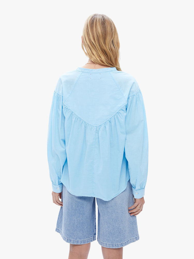 Back view of a woman in XiRENA loose, flowy top that has a buttoned v-neck, long balloon sleeves and ruffles throughout for a voluminous fit in a baby blue hue