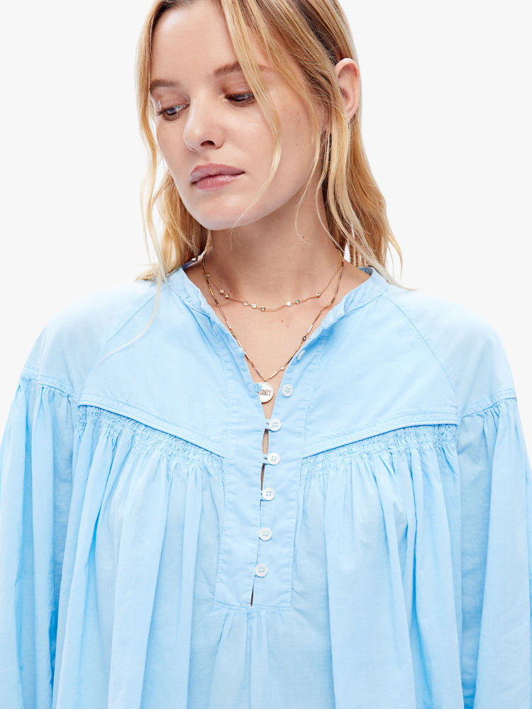 Close up view of a woman in XiRENA loose, flowy top that has a buttoned v-neck, long balloon sleeves and ruffles throughout for a voluminous fit in a baby blue hue