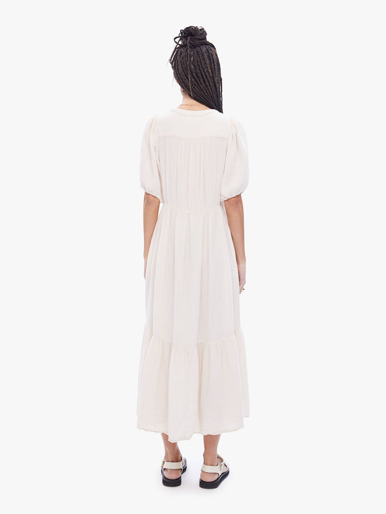Back full body view of a woman in a maxi dress from XiRENA, the dress features a Vneck, short balloon sleeves and flowy tiered skirt in an off- white hue