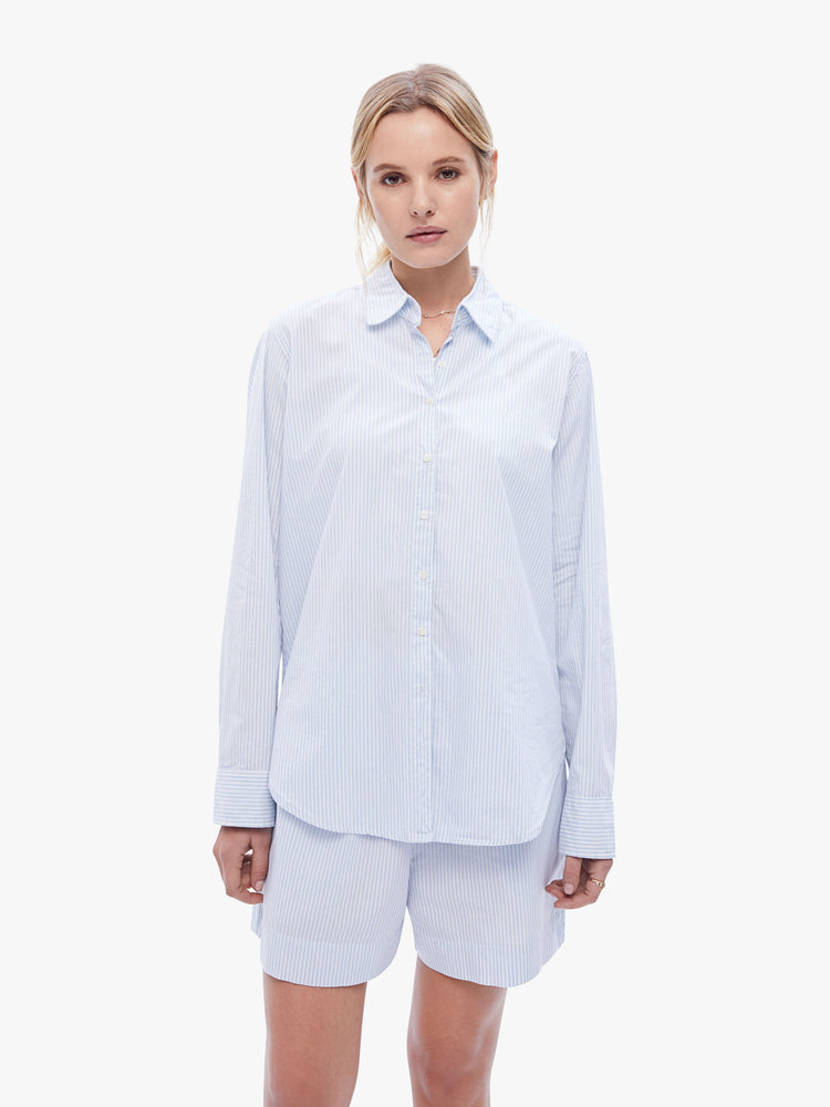 Front view of a woman in a classic button down with a sky blue stripe pattern, the long sleeve shirt features a Vneck, curved hem and oversized fit