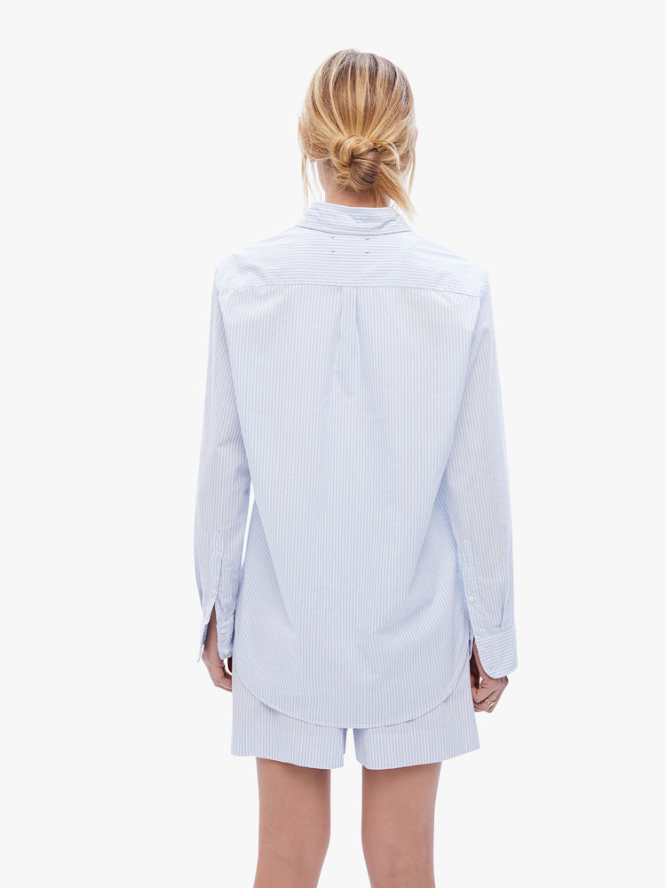 Back view of a woman in a classic button down with a sky blue stripe pattern, the long sleeve shirt features a Vneck, curved hem and oversized fit