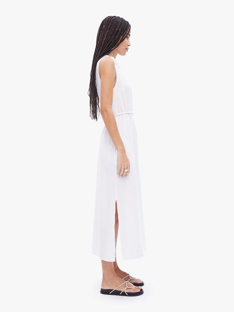 Side full body view of a woman in a sleeveless maxi dress from XiRENA, dress is made from 100% cotton in white and features a ruffled crewneck, tied waist, ankle length hem and effortless vibe