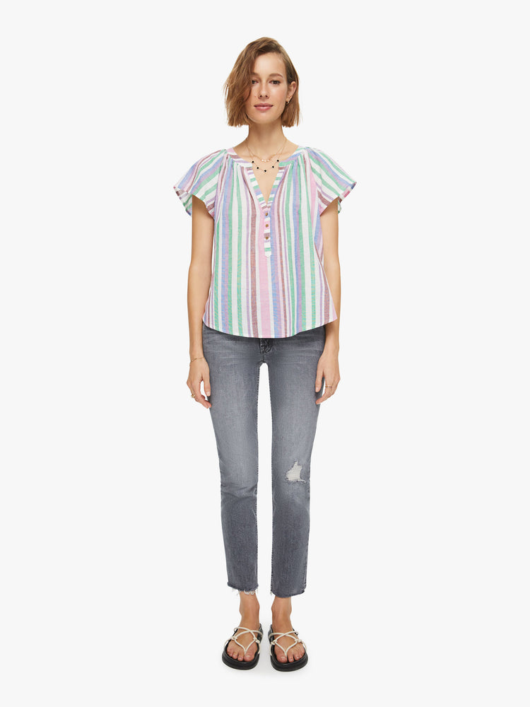 Full body view of a woman in a 100% cotton in a baby pink, periwinkle and mint green stripe pattern, the Kimber top is designed with a buttoned V-neck, drop shoulders and a curved hem with side slits.