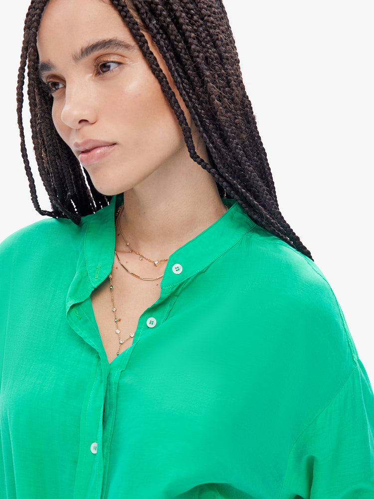 Close up front view of a woman in Xirena long sleeve mini dress made from a blend of cotton and silk in a bright green hue, and features a vneck, buttons down the front and a layered, gathered skirt that ties at the waist.