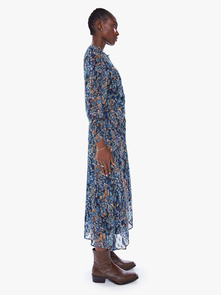 Side full body view of a woman in blue floral print midi dress by Maria Cher that features a V-neck, gathered bodice, puffed shoulders and slightly cropped long sleeves
