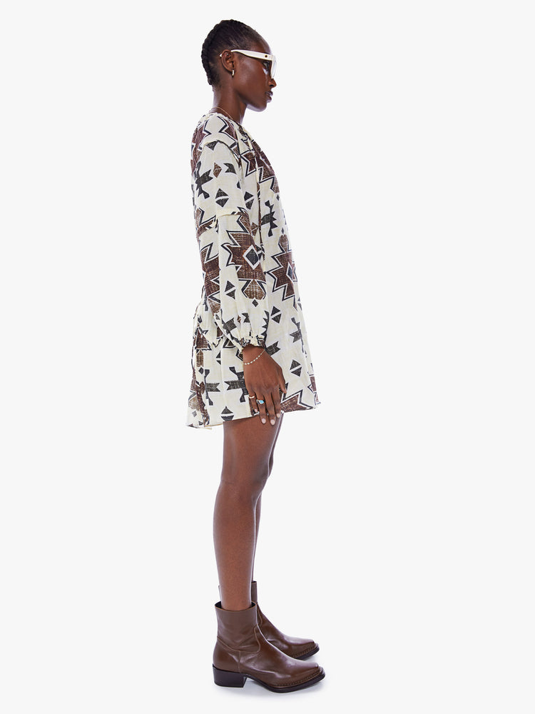 Side view of a woman in long sleeve mini dress from Maria Cher which reinterprets classic styles with bold prints and modern neutrals, the dress is made from a blend of cotton and silk in white with a dark pattern and features a Vneck, long balloon sleeves and a slightly curved hem that hits mid thigh