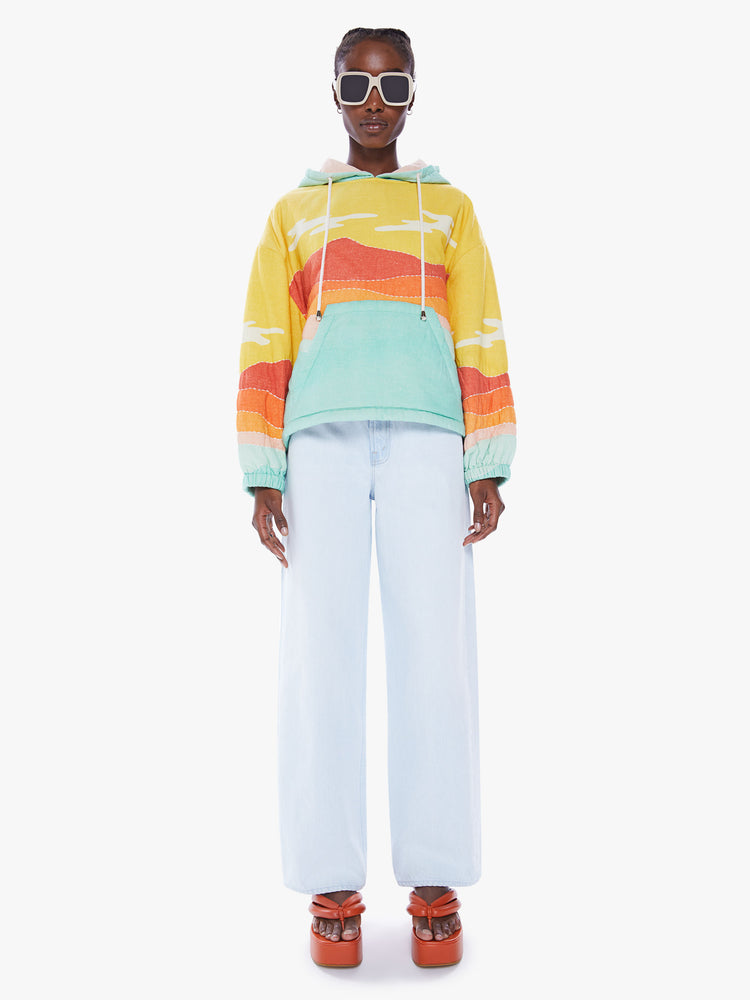 Full body view of a woman in a colorful hoodie from Arizona Love, a french brand that combines a nomadic spirit with chic Parisian style, sweatshirt made from 100% cotton with yellow, orange and blue desert quilted graphic, features a drawstring hood, long sleeves with elastic hem an oversized front patch pocket and a boxy fit
