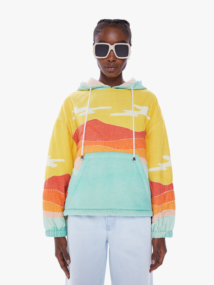 Front view of a woman in a colorful hoodie from Arizona Love, a french brand that combines a nomadic spirit with chic Parisian style, sweatshirt made from 100% cotton with yellow, orange and blue desert quilted graphic, features a drawstring hood, long sleeves with elastic hem an oversized front patch pocket and a boxy fit