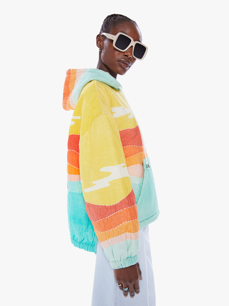Side view of a woman in a colorful hoodie from Arizona Love, a french brand that combines a nomadic spirit with chic Parisian style, sweatshirt made from 100% cotton with yellow, orange and blue desert quilted graphic, features a drawstring hood, long sleeves with elastic hem an oversized front patch pocket and a boxy fit