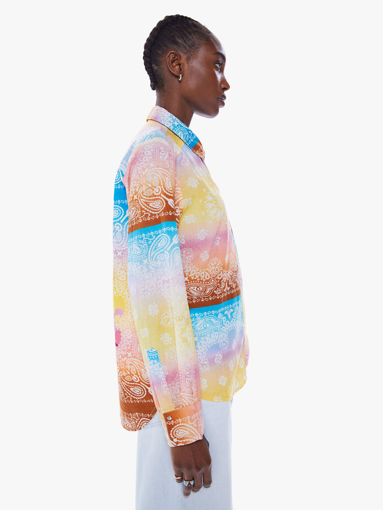 Side view of a woman in a handcrafted button up shirt from Arizona Love, a French brand that combines a nomadic spirit with chic Parisian style, the shirt is made from 100% cotton bandanas tie-dyed in pastel rainbow hues and features long sleeve, a curved hem and slightly loose fit