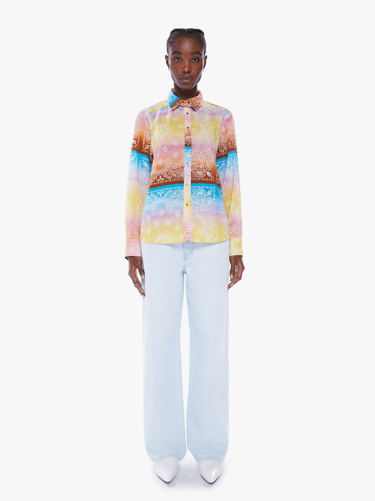 Full body view of a woman in a handcrafted button up shirt from Arizona Love, a French brand that combines a nomadic spirit with chic Parisian style, the shirt is made from 100% cotton bandanas tie-dyed in pastel rainbow hues and features long sleeve, a curved hem and slightly loose fit