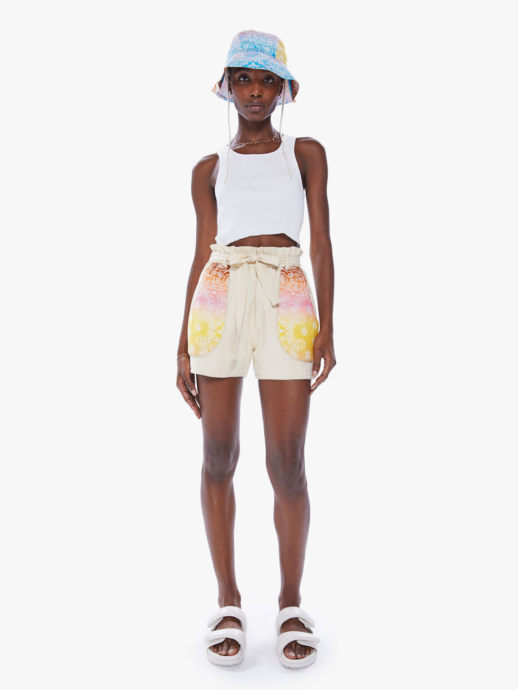 Front view of a woman in a high waisted shorts made from 100% cotton in a khaki hue and feature a tied paper bag waist, front patch pockets designed from pastel tie dyed bandanas and a slightly loose fit from Arizona Love.