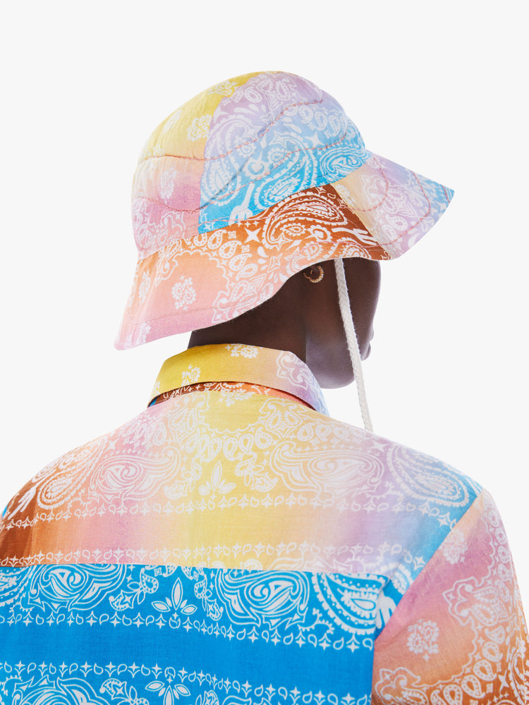 Back view of a woman in a wide-brim bucket hat from Arizona Love, a French accessories brand that combines a nomadic spirit with chic Parisian style made from 100% cotton bandanas tie-dyed in pastel rainbow hues
