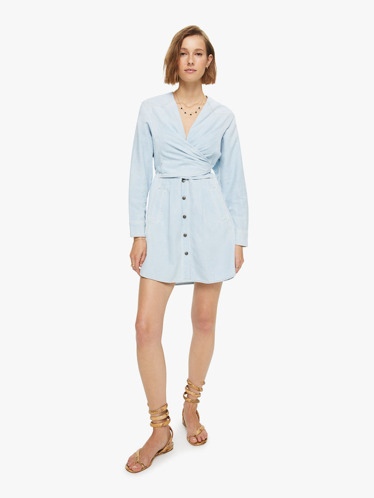 Front view Sandrine dress features a V-neck, wrapped bodice, 3/4-length sleeves with gathered elastic hems and a buttoned skirt with front pockets. Made of 100% cotton in a light blue chambray, the dress is soft and lightweight.