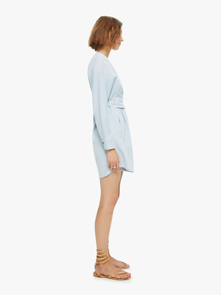 Side view Sandrine dress features a V-neck, wrapped bodice, 3/4-length sleeves with gathered elastic hems and a buttoned skirt with front pockets. Made of 100% cotton in a light blue chambray, the dress is soft and lightweight.