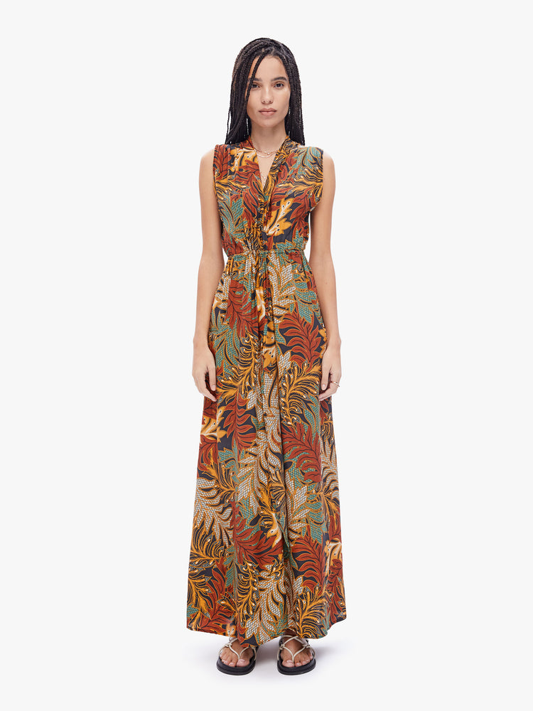 Front full body view of a woman in a Nico dress created by Natalie Martin, made from 100% silk in a brown, green, burnt orange and cream leaf print, and features a V-neck, fitted waist and ankle-length hem