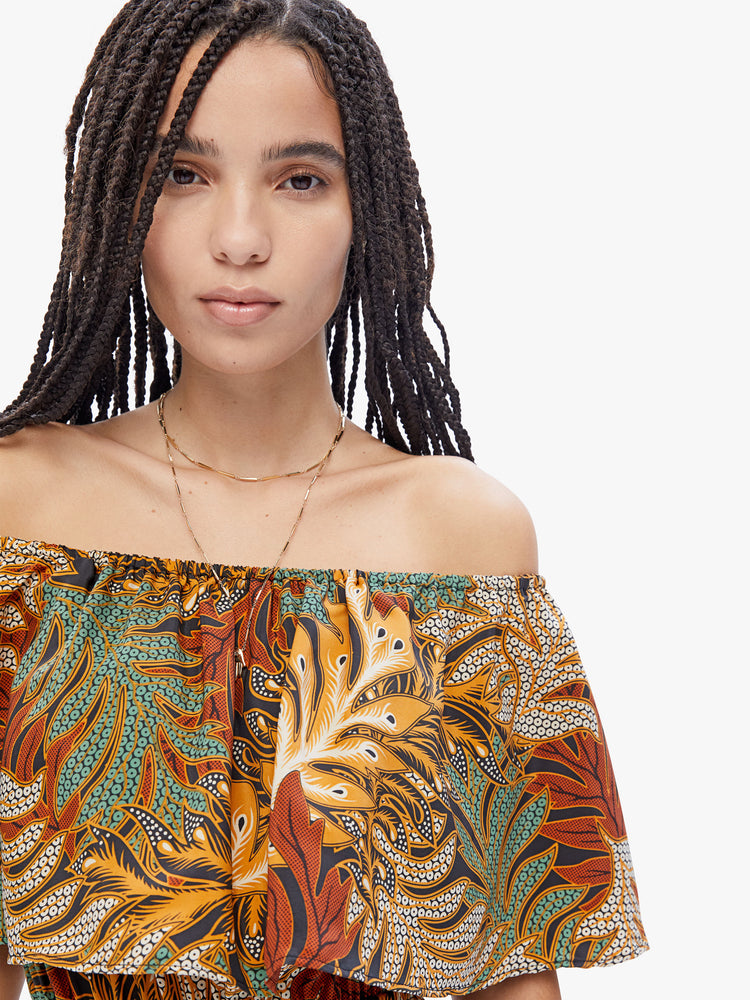 Close up neckline view of a woman in a Naomi dress by Natalie Martin made from 100% silk in a brown, green, burnt orange and cream leaf print. Maxi dress features an off the shoulder elastic neckline with an oversized ruffle, a fitted waist and a tiered ankle-length skirt