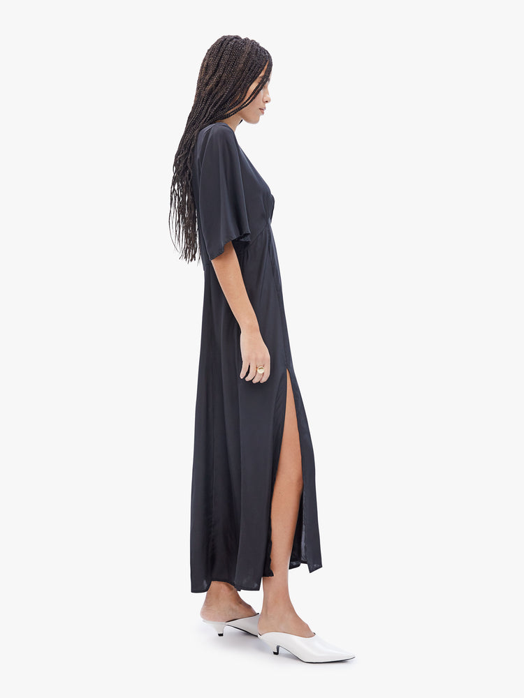 Side  full body view of a woman in maxi dress made from 100% silk in black, features a crewneck, flowy elbow-length sleeves, a gathered curved waist and an ankle length hem