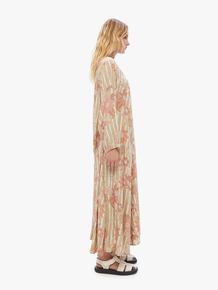 Side view of woman maxi dress with an A-line cut and voluminous sleeves in a tan stripe pattern with warm-toned sunflowers.