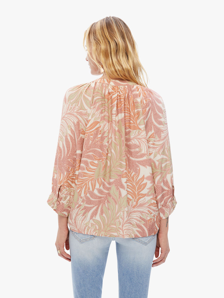 Back view of a woman top with a V-shaped neckline with covered buttons and subtle pleats below the collar emphasizes the loose in a pink and orange leaf print.