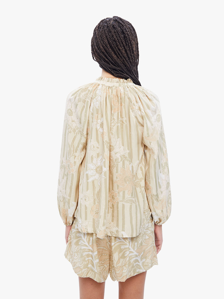 Back view of a woman top with a keyhole neckline with a tasseled tie closure, long balloon sleeves and pleats for a loose fit in a cream stripe pattern with tonal sunflowers.