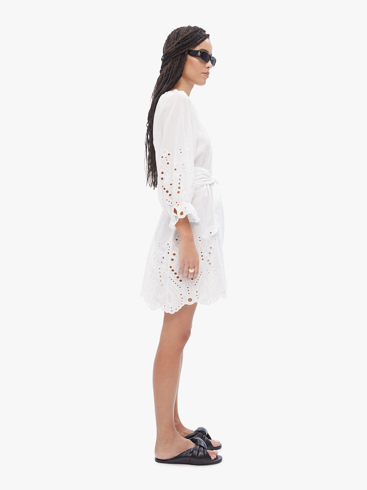 Side view of a woman's mini dress is designed with a rounded square neck, buttons down the front, cropped balloon sleeves and a tied waist in a salt white with oversized eyelet.