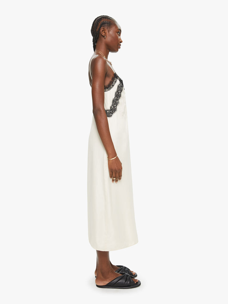 Side view of a woman white with black lace details slip dress features a V-neck with buttons, spaghetti straps and a loose fit.