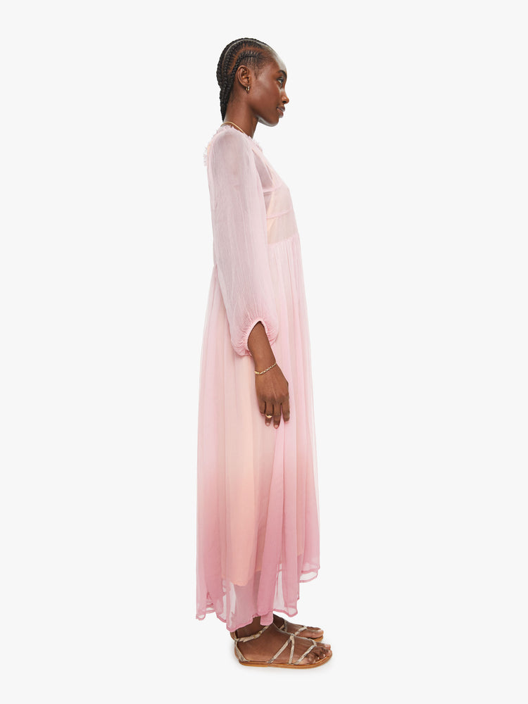 Side view of a woman baby pink ombre hue maxi dress with ruffled crewneck, cropped sleeves, gathered waist and uneven hem.