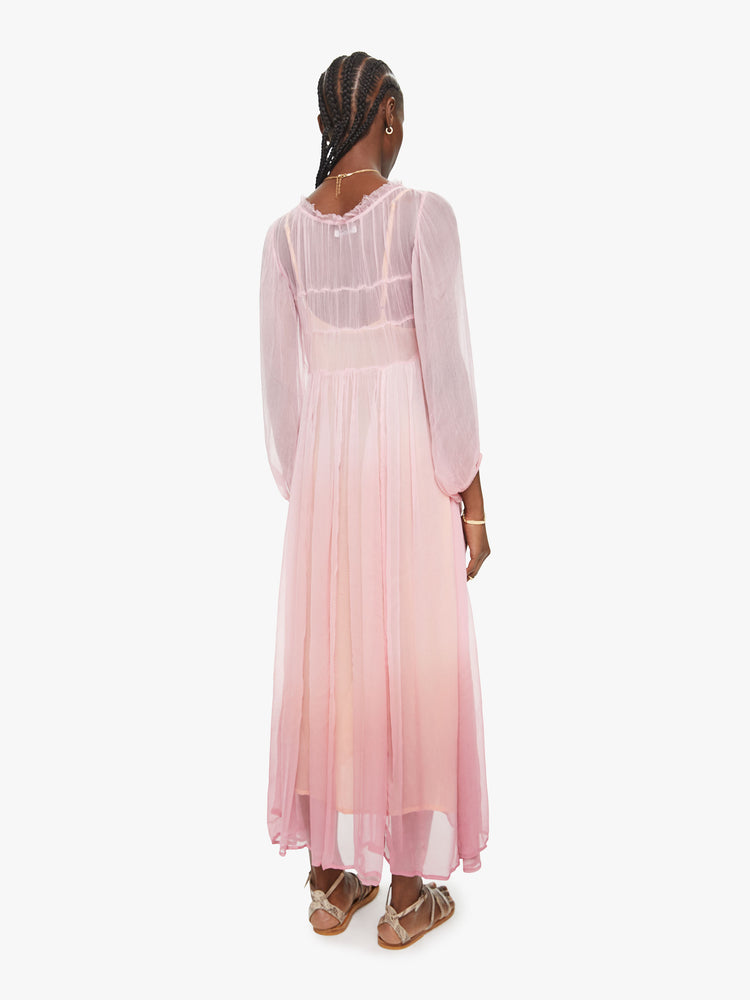 Back view of a woman baby pink ombre hue maxi dress with ruffled crewneck, cropped sleeves, gathered waist and uneven hem.