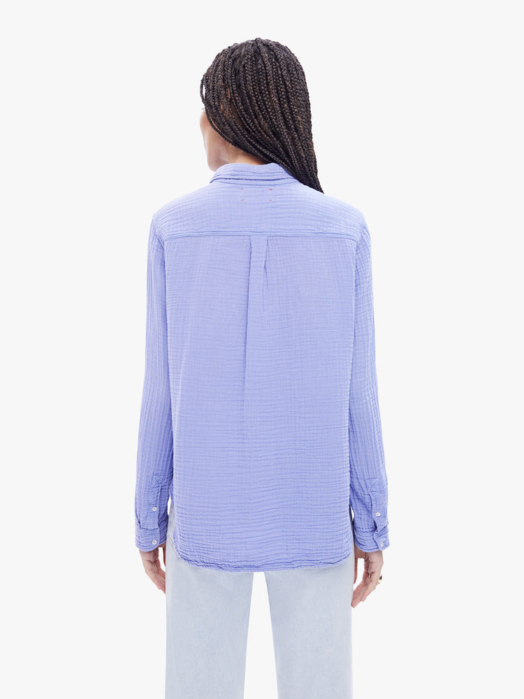 Back view of a woman in periwinkle button down from XiRENA made from 100% cotton, the long sleeve shirt features a Vneck and curved hem with a light and airy fit